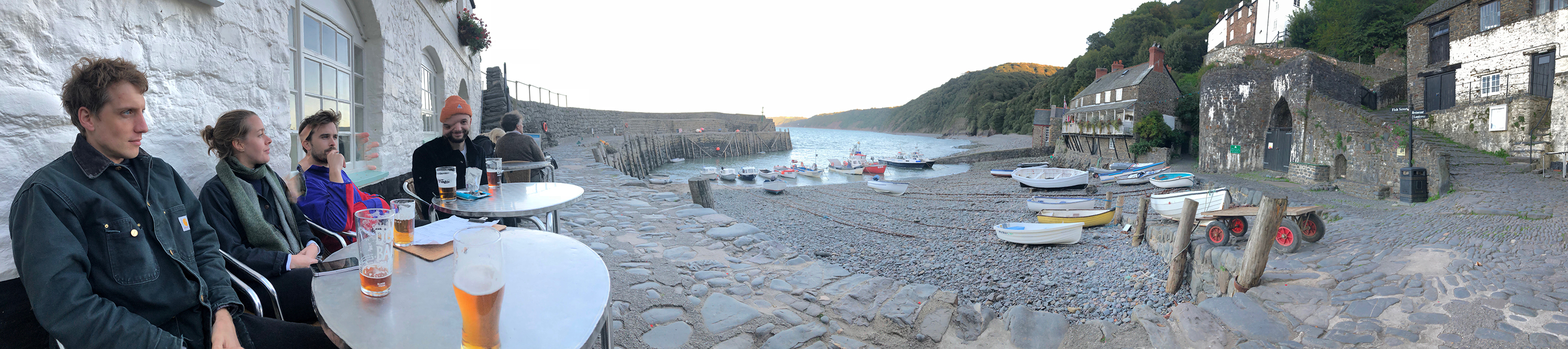 Panoramic photo of friends with pints in Clovelly Bay, Devon