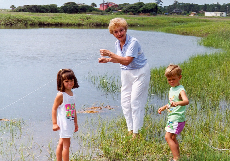 A grandmother in white trousers crabbing with her two four-year-old grandkids