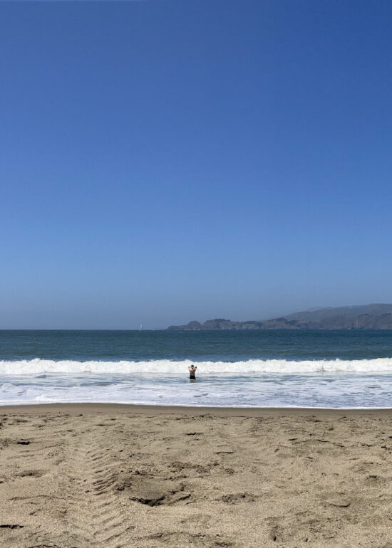 A distant woman standing in the surf at Baker Beach