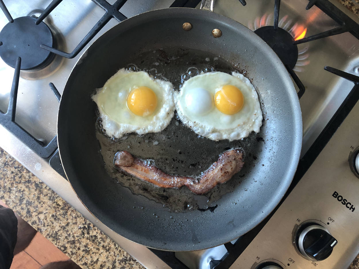 A bird’s-eye view of eggs and bacon in a pan arranged like a smiley face