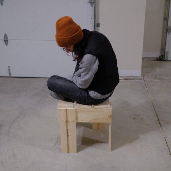 A woman in an orange beanie sitting on a pine stool made in Rietveld’s crate style