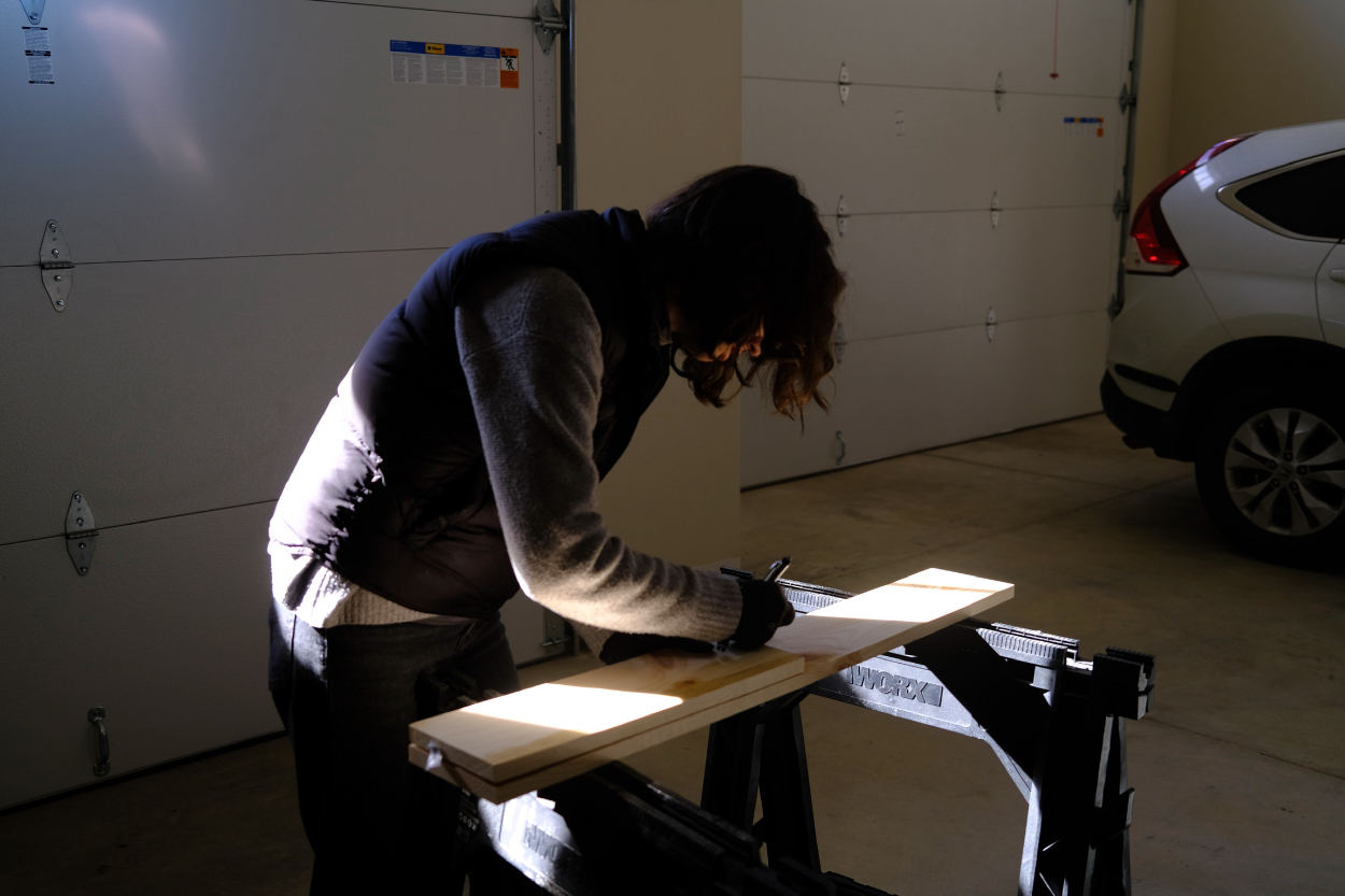 Woman working marking a plank of wood in a garage