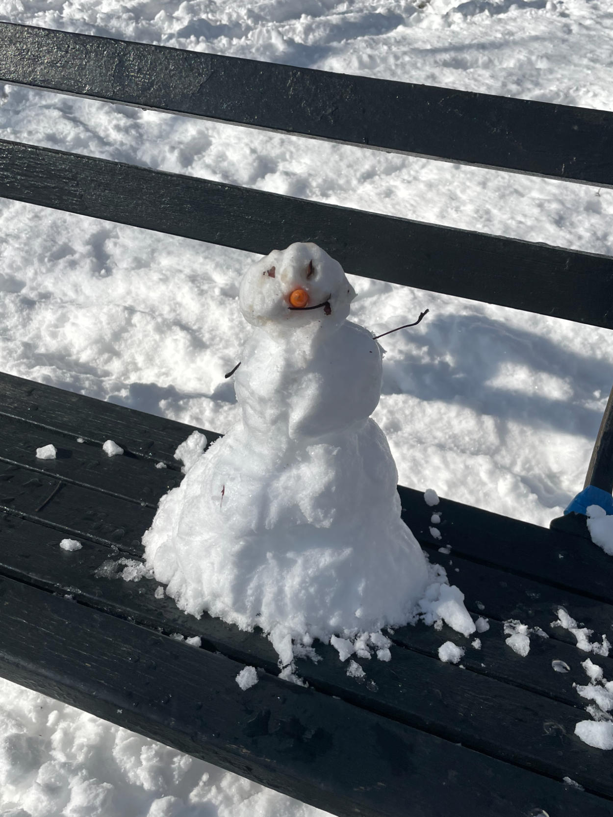 A small snowman sitting on a black bench