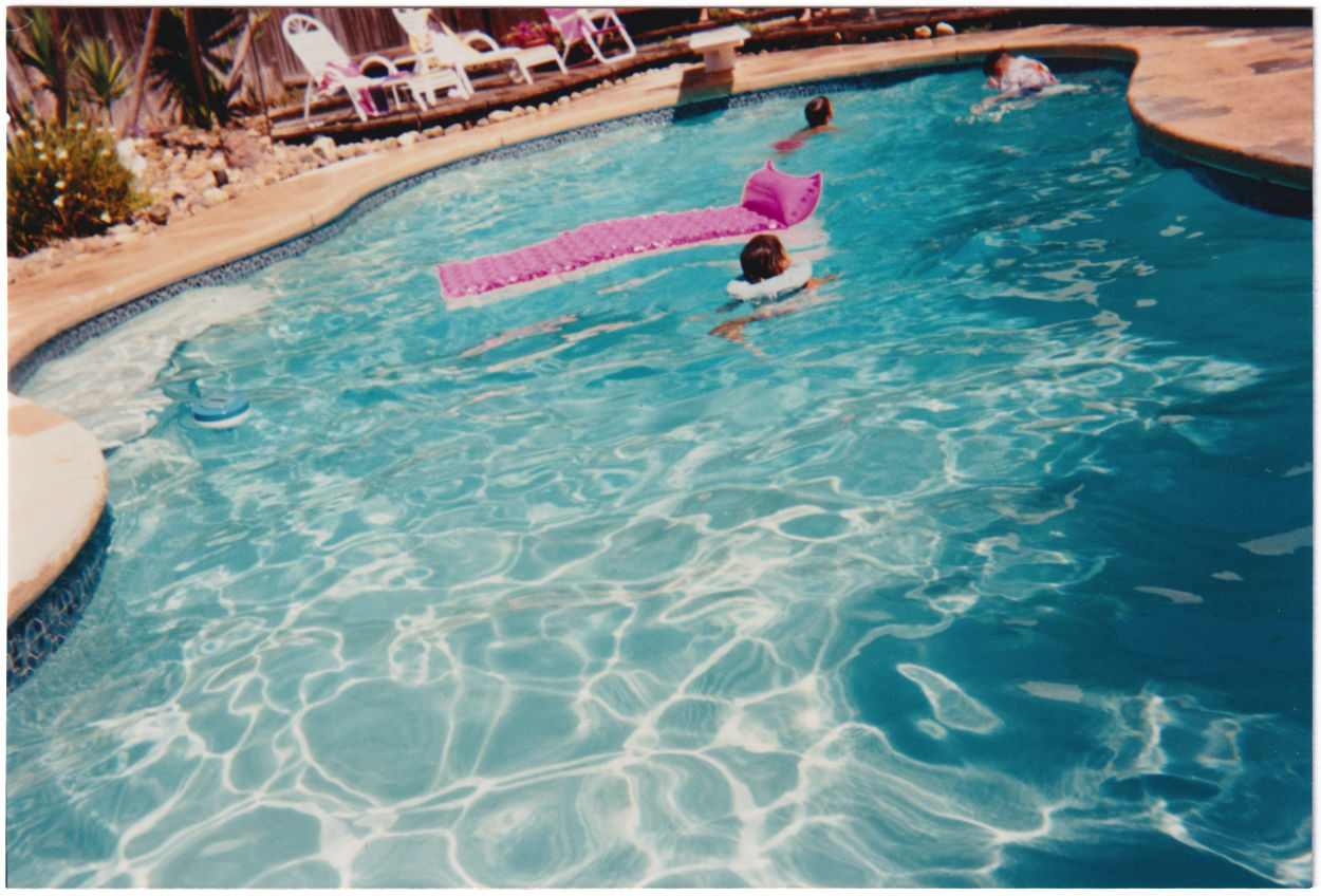 Three kids in a kidney-shaped pool with cyan water and a bright pink floatie