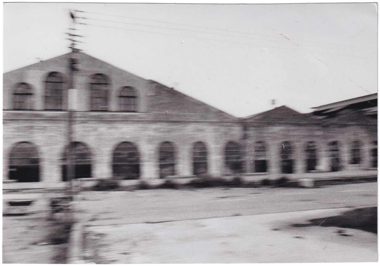 Black and white photo of a low warehouse with arched windows, with motion blur